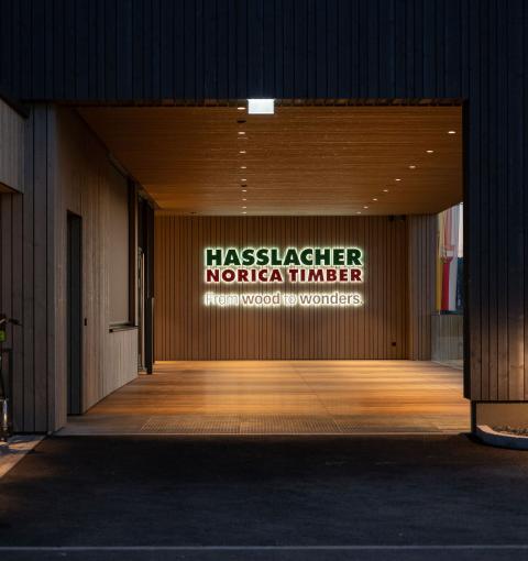 The new office building of HASSLACHER PREDING Holzindustrie in the evening with entrance area and illuminated logo